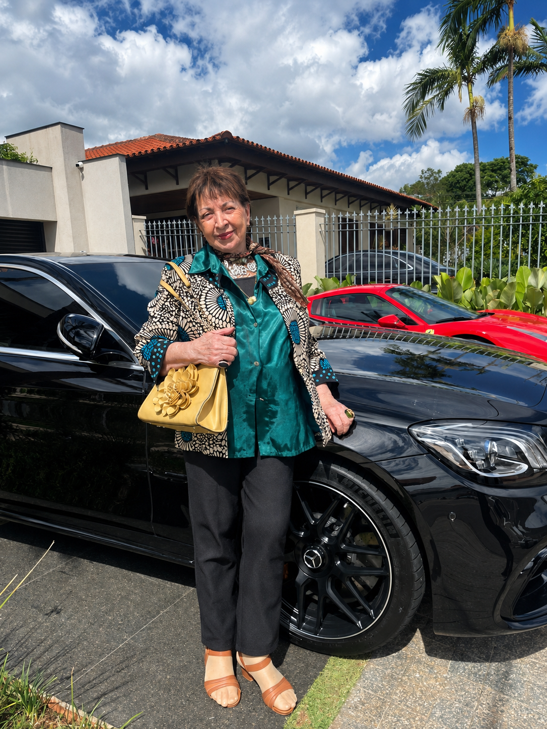 Marlene Galeazzi posando ao lado de um carro preto com outro carro vermelho ao fundo em Dubai.