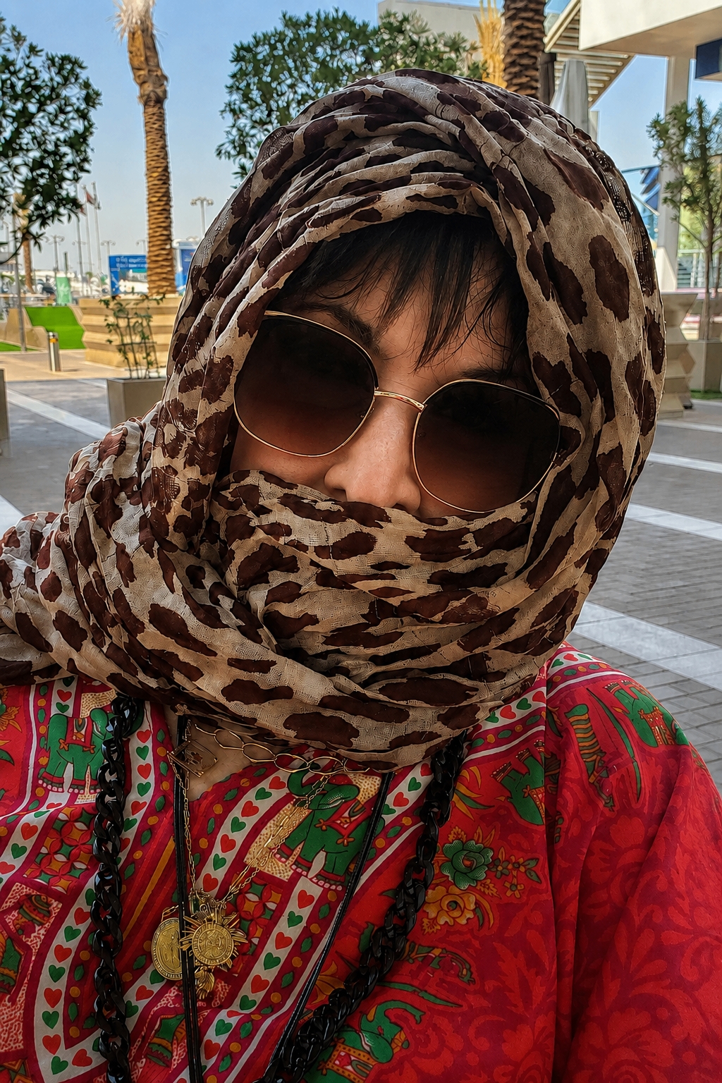 Close de Marlene Galeazzi com lenço estampado cobrindo parte do rosto e óculos escuros em Dubai.